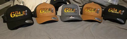 Six trucker caps in black, caramel and charcoal, each embroidered with the yellow and orange Gila Monster logo