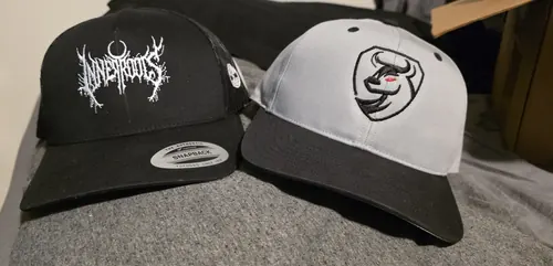 A black trucker with the white Inner Roots logo next to a grey and black two-tone cap with a bull shield logo