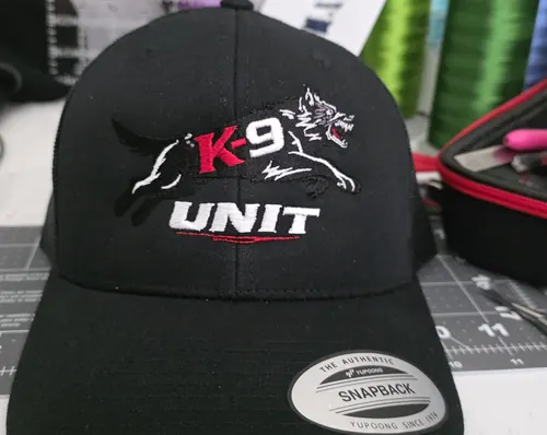 Black Yupoong trucker with a K-9 Unit logo: a white wolf, red K-9 and white UNIT